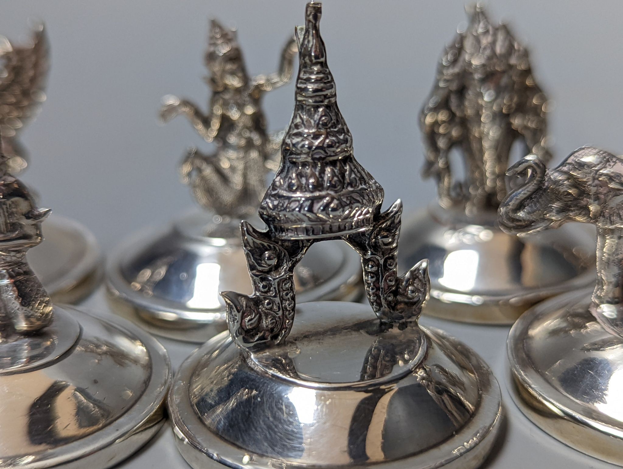 Sixteen assorted Siamese sterling mounted menu holders, modelled with figures, elephant, etc.